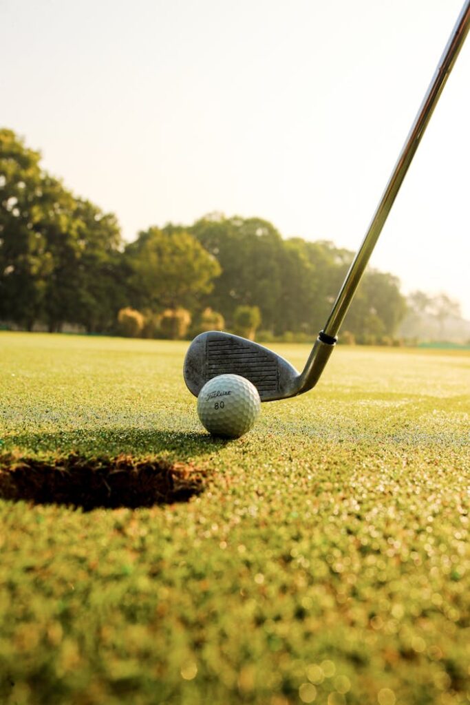 Closeup of golf ball placed on green grassy court against golf club under clear blue sky on sunny day