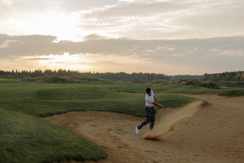Golfer hitting a sand shot at sunset on a scenic golf course, showcasing skill and landscape.